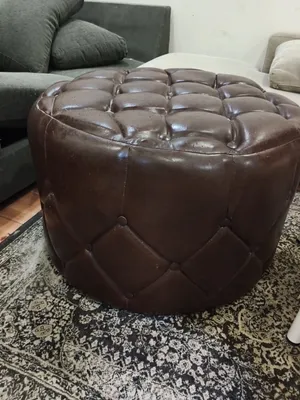This product is a round leather pouf/footrest with a quilted design and button details. Features and