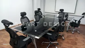ترابيزة اجتماعات زجاجية بتصميم مودرن وأنيق، مع كراسي مريحة بشبك وظهر داعم للرأس، مثالية لقاعات